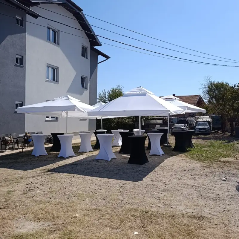 Barski stolovi s crnim i bijelim navlakama ispod suncobrana pored zgrade